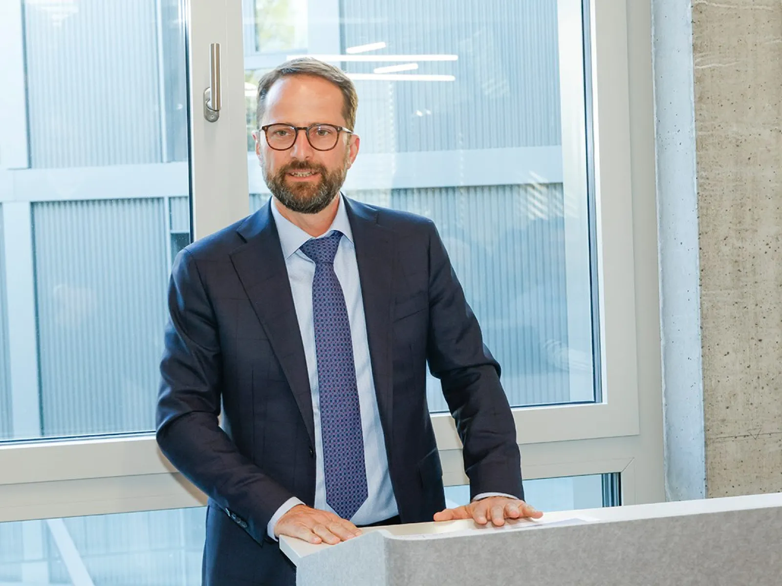 Ein Mann im Anzug steht an einem Rednerpult vor einem Fenster.
