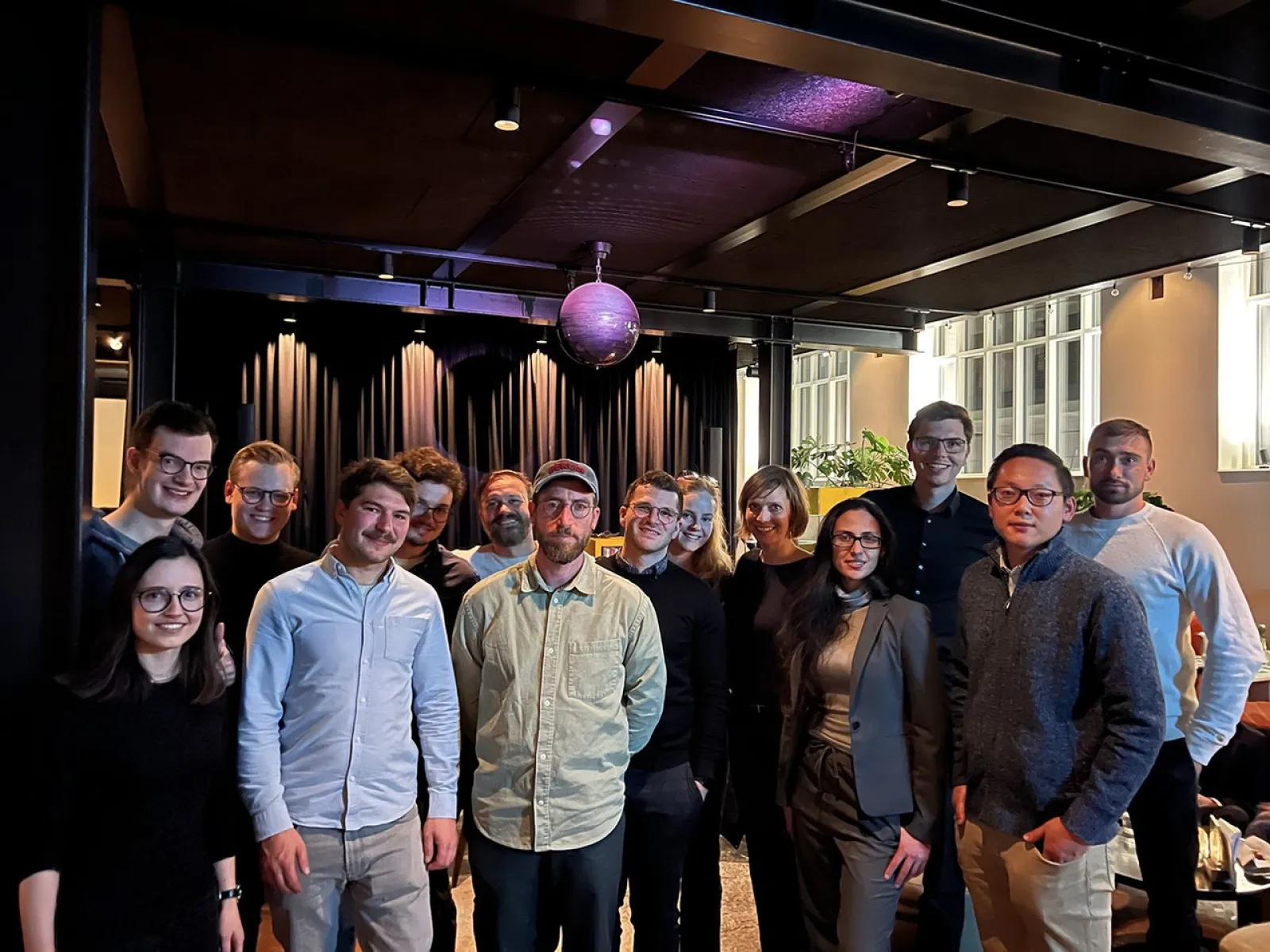 Eine Gruppe von Alumni der Universität Liechtenstein steht lächelnd in einem modernen Veranstaltungsraum zusammen. Im Hintergrund sind eine Bühne und eine Discokugel zu sehen.