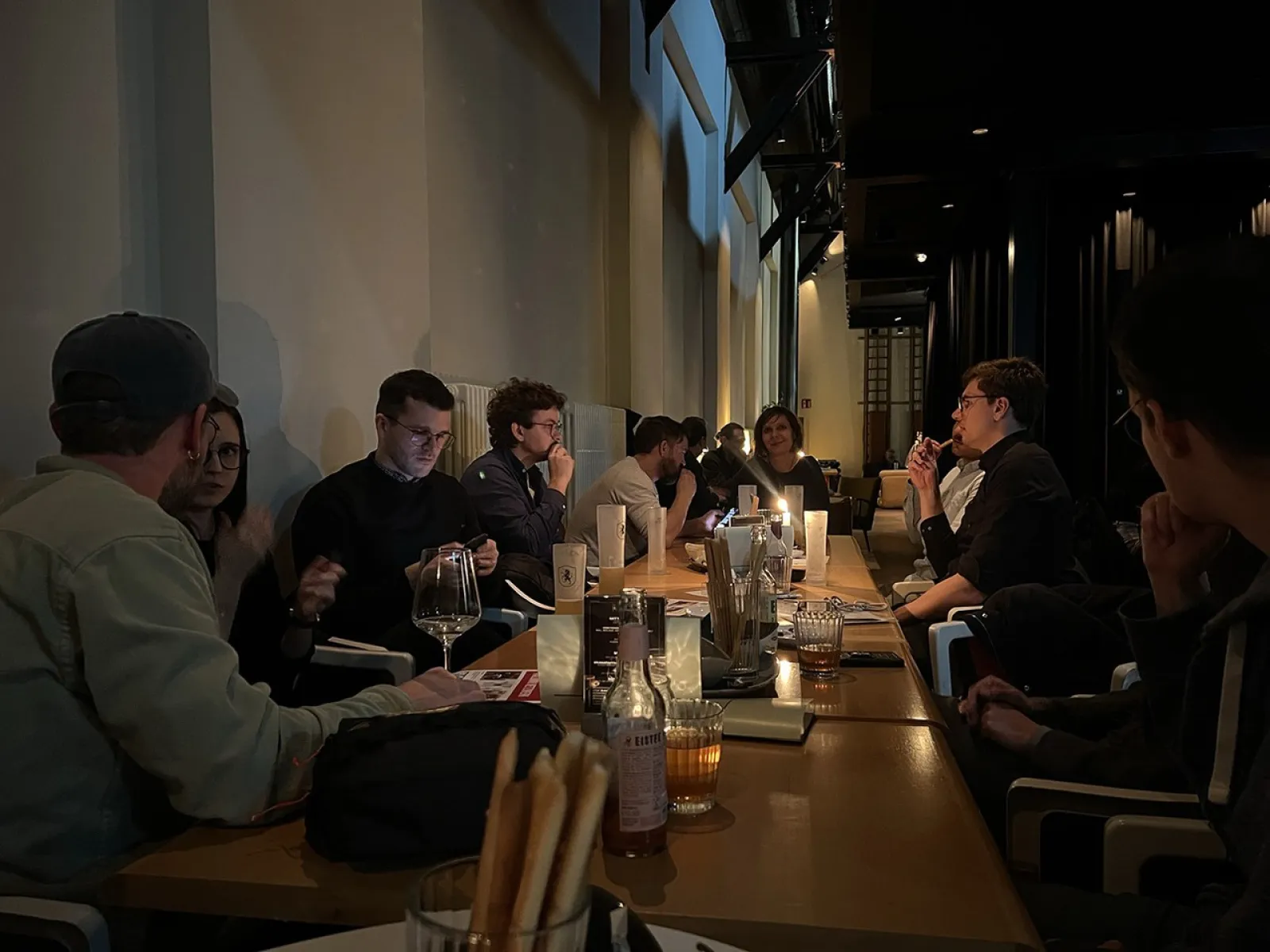 Alumni-Treffen in einem gemütlichen Restaurant: Eine Gruppe von Menschen sitzt an einem langen Tisch, unterhält sich und genießt Getränke in entspannter Atmosphäre.