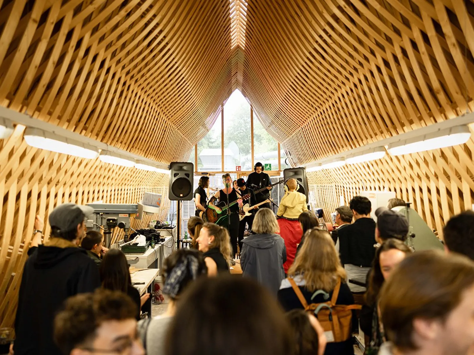 Eine Band spielt vor einem Publikum in einem architektonisch beeindruckenden Raum mit Holzgitterstruktur bei einem Event der Universität Liechtenstein.