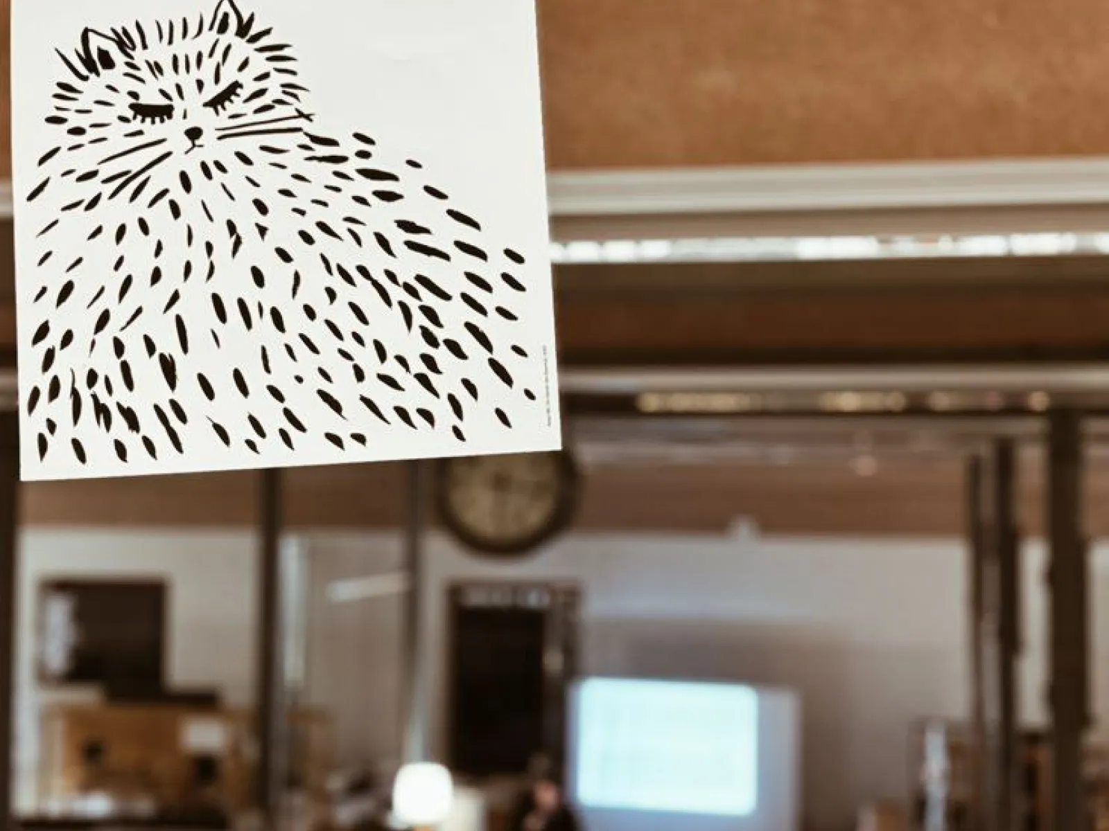 Ein handgezeichnetes Bild einer flauschigen Katze mit dem Text "I don't want to talk about it" hängt vor einem unscharfen Hintergrund, der einen Raum mit einer Präsentation zeigt.