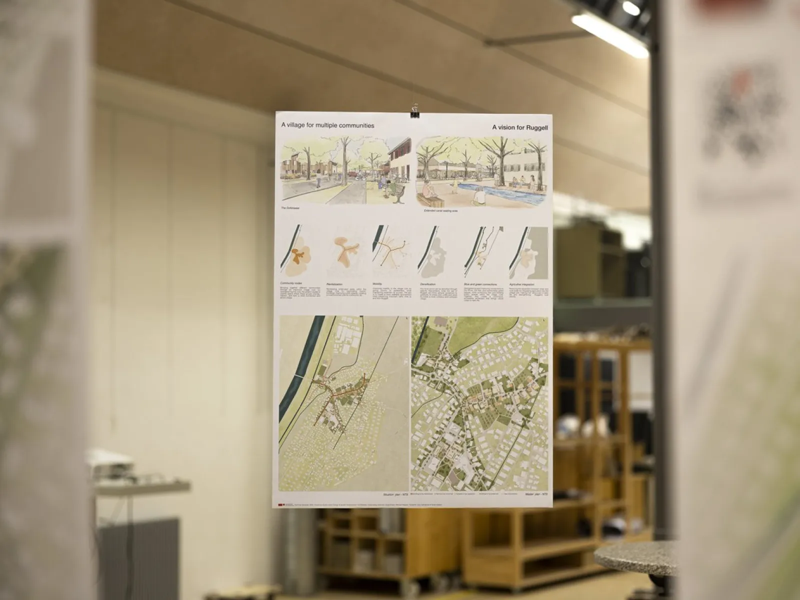 Ein Poster hängt in einem Innenraum und zeigt architektonische Pläne und Illustrationen. Es enthält Karten und Diagramme, die Konzepte für nachhaltiges Bauen darstellen. Der Hintergrund ist unscharf, was den Fokus auf das Poster lenkt.
