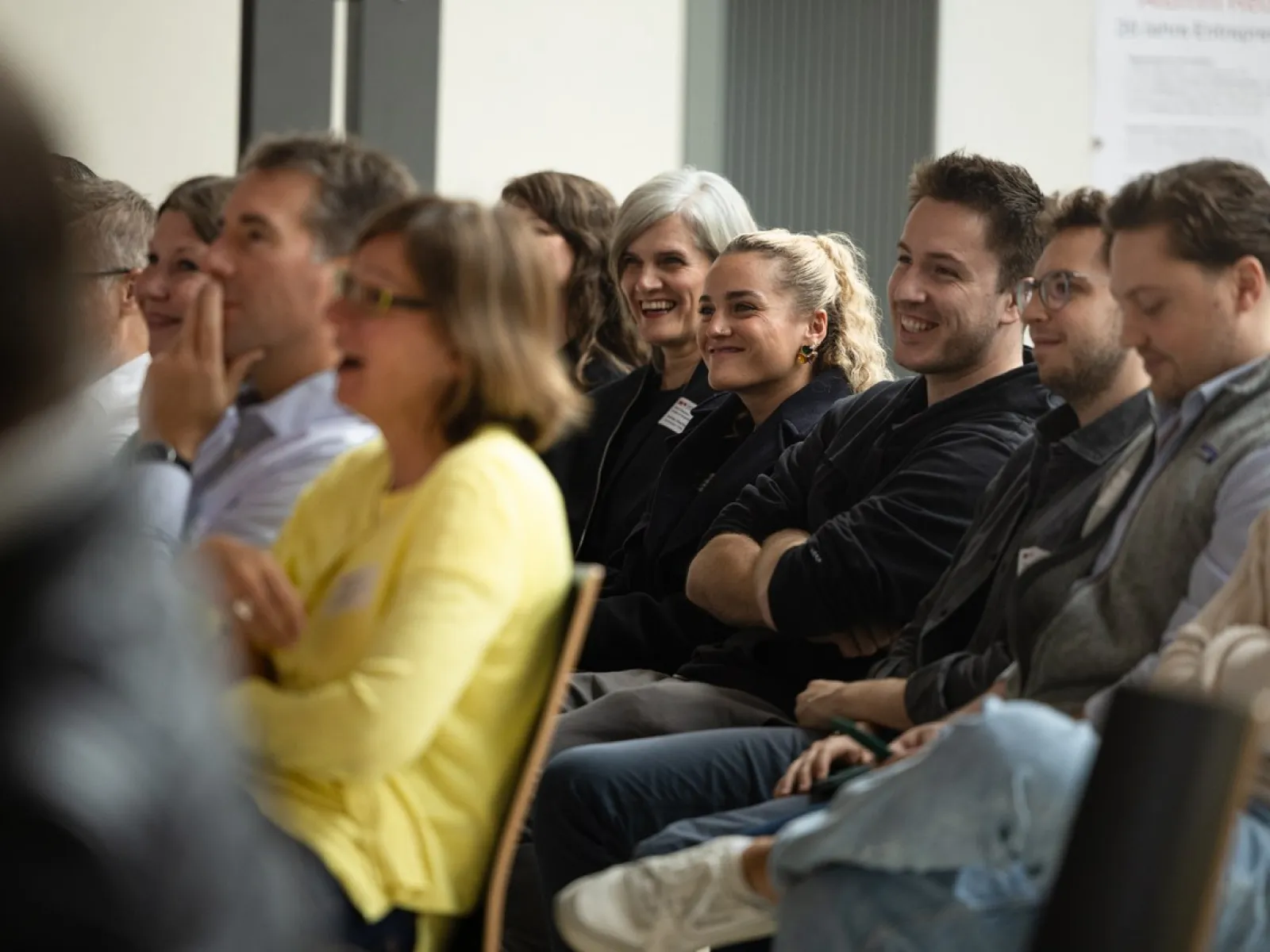 Eine Gruppe von Menschen sitzt in einem Auditorium und lächelt während einer Veranstaltung an der Universität Liechtenstein. Die Atmosphäre wirkt entspannt und fröhlich.