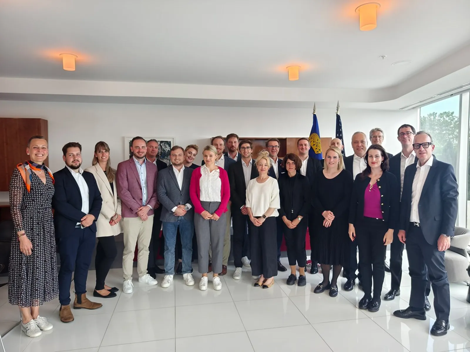 Gruppe von Studierenden und Dozenten des Executive Master of Laws (LL.M.) der Universität Liechtenstein während einer Studienreise in einem modernen Konferenzraum, im Hintergrund Flaggen.