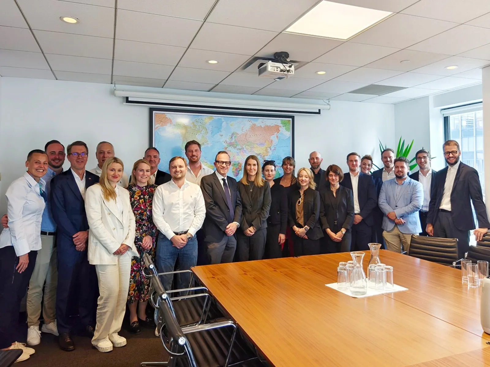Gruppenfoto von Studierenden und Dozenten des Executive Master of Laws (LL.M.) während einer Studienreise in einem Konferenzraum mit Weltkarte im Hintergrund.