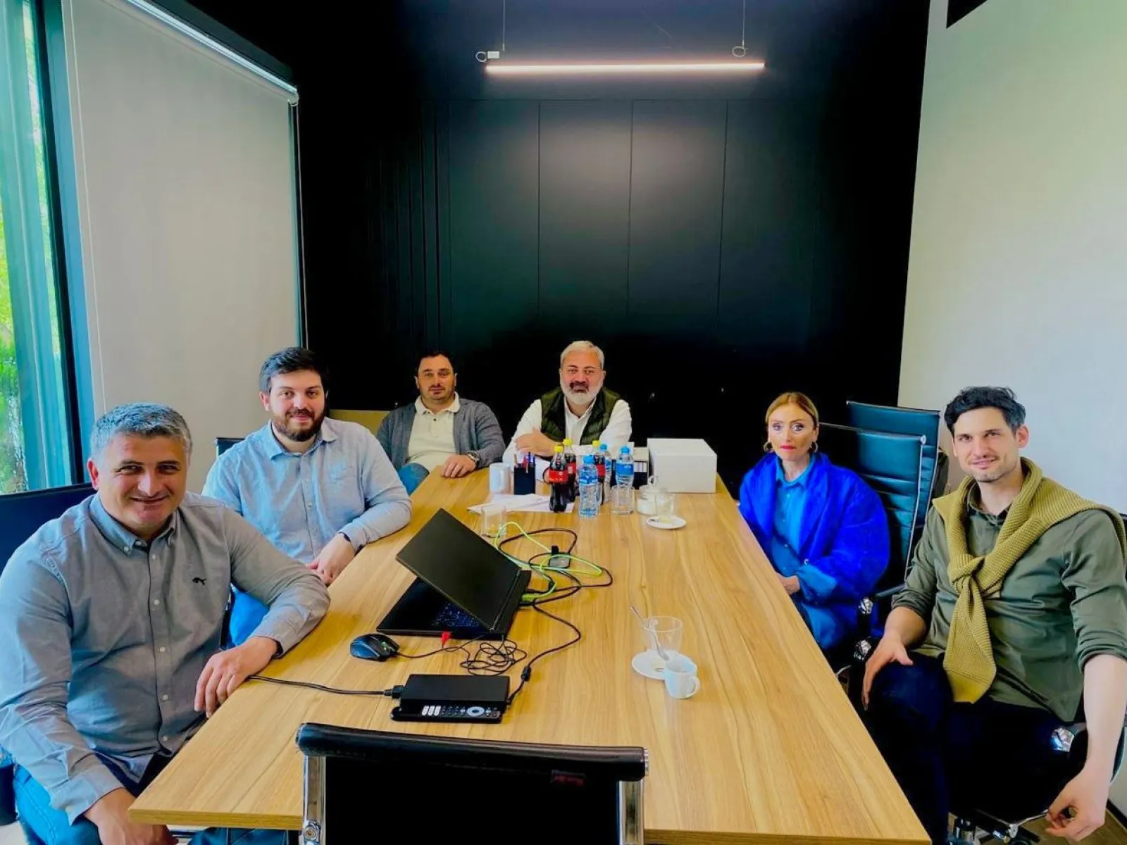 Sechs Personen sitzen an einem Besprechungstisch in einem modernen Konferenzraum und nehmen an einem Meeting oder Workshop teil.
