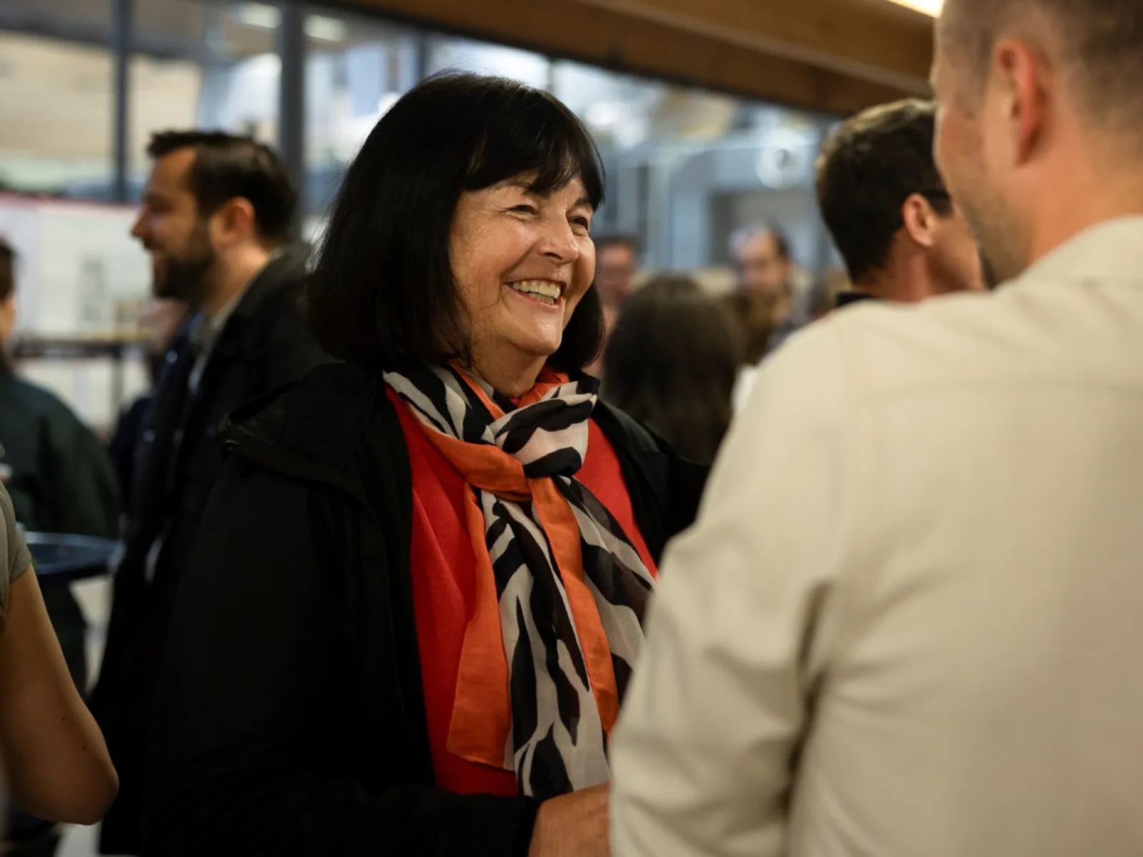 Eine Person lächelt und unterhält sich mit einer anderen Person in einem belebten Raum während des LSA Sommerfests an der Universität Liechtenstein. Im Hintergrund sind weitere Gäste zu sehen.