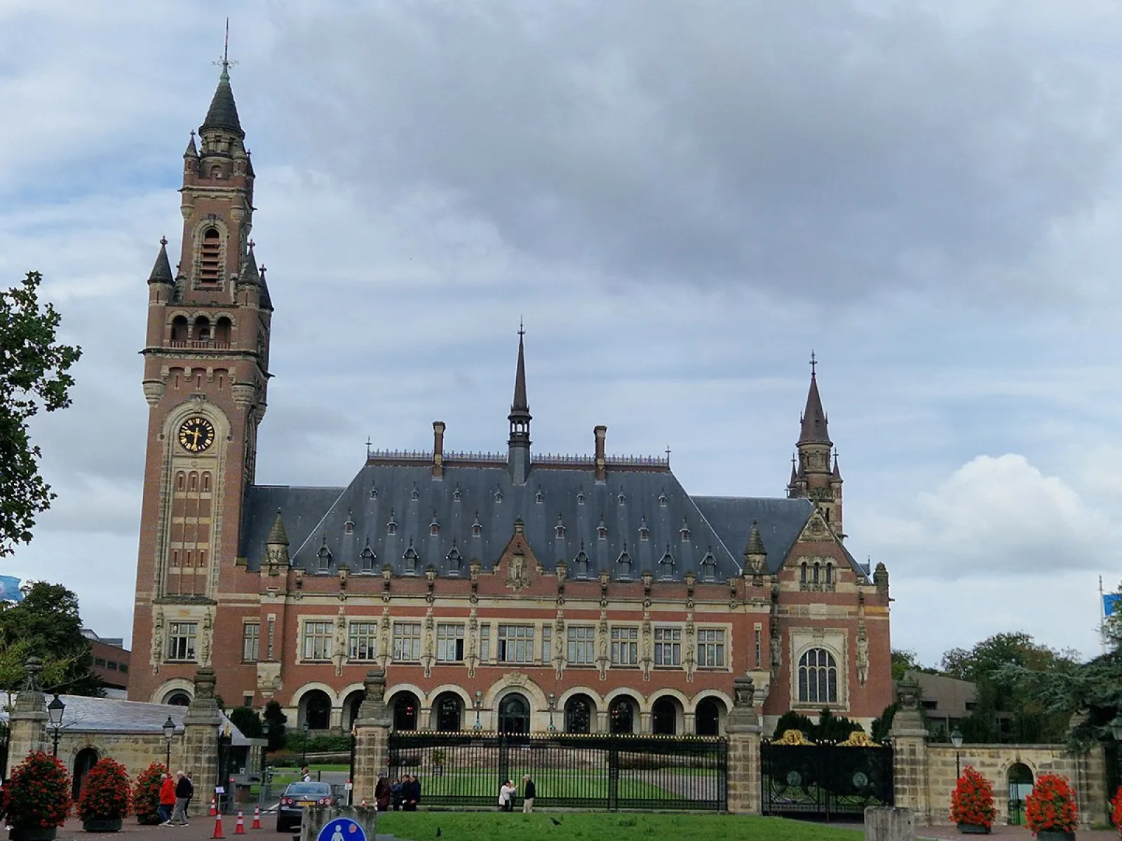 Der Friedenspalast in Den Haag, ein beeindruckendes historisches Gebäude mit einem großen Turm und einer gepflegten Gartenanlage, unter einem bewölkten Himmel.