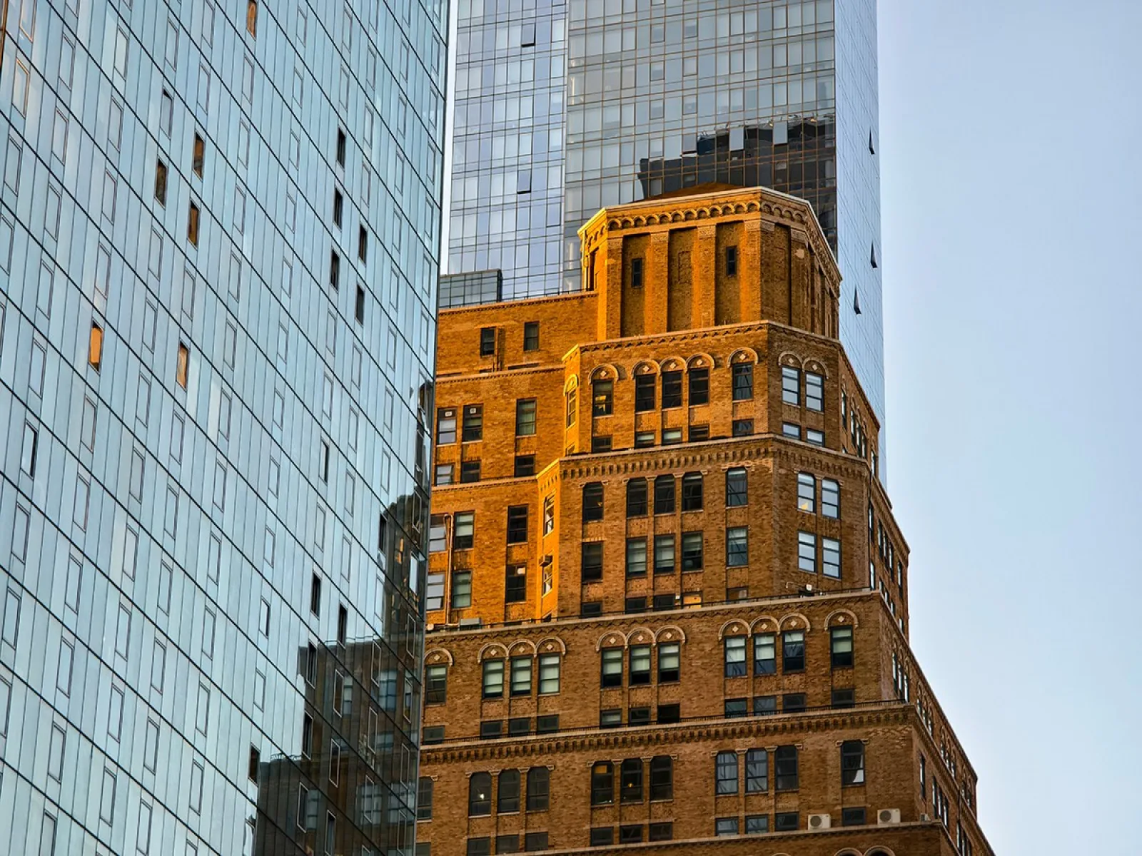 Moderne und historische Architektur in New York City, mit einem markanten Backsteingebäude im Vordergrund und gläsernen Hochhäusern im Hintergrund. Symbolisiert den Kontrast und die Vielfalt der Stadt.