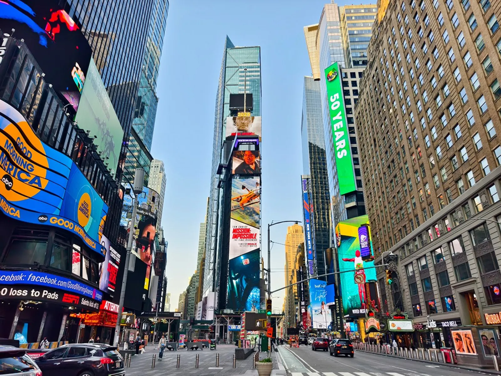 Blick auf den belebten Times Square in New York City mit hohen Gebäuden und leuchtenden Werbetafeln. Menschen und Autos beleben die Szene.