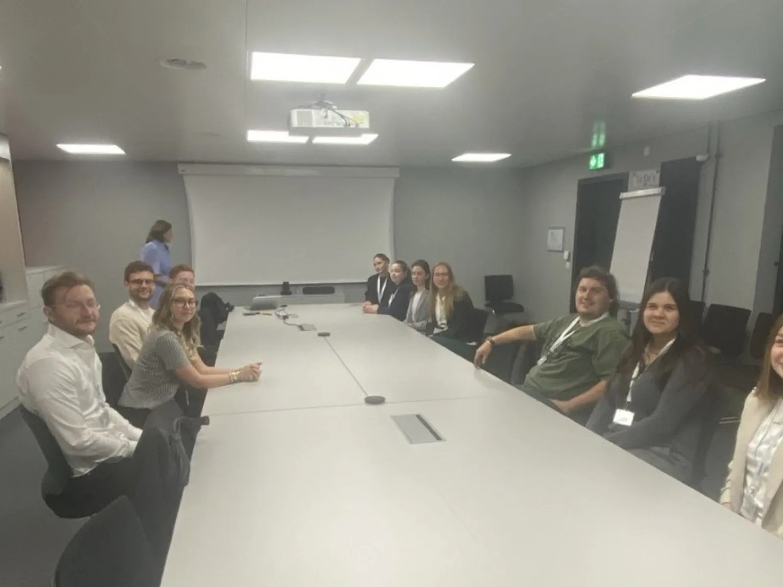 Studierende der Universität Liechtenstein sitzen in einem Konferenzraum bei Ivoclar in Schaan. Im Hintergrund ist eine Präsentationsleinwand zu sehen.