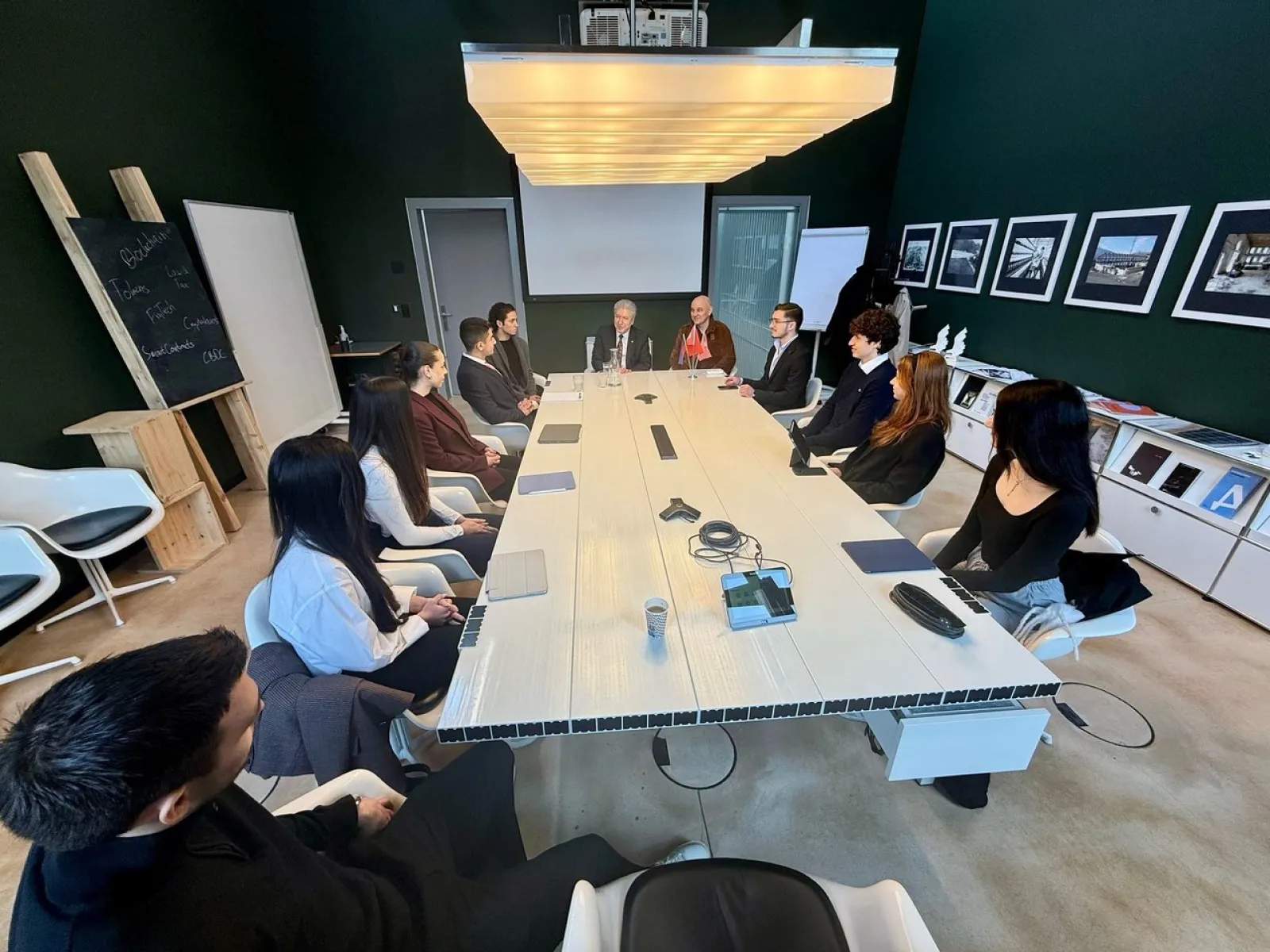 Besprechung in einem modernen Konferenzraum an der Universität Liechtenstein. Eine Gruppe von Personen sitzt um einen langen Tisch, darunter akademische Vertreter und Studierende. An den Wänden hängen Bilder, und im Raum steht eine Tafel.