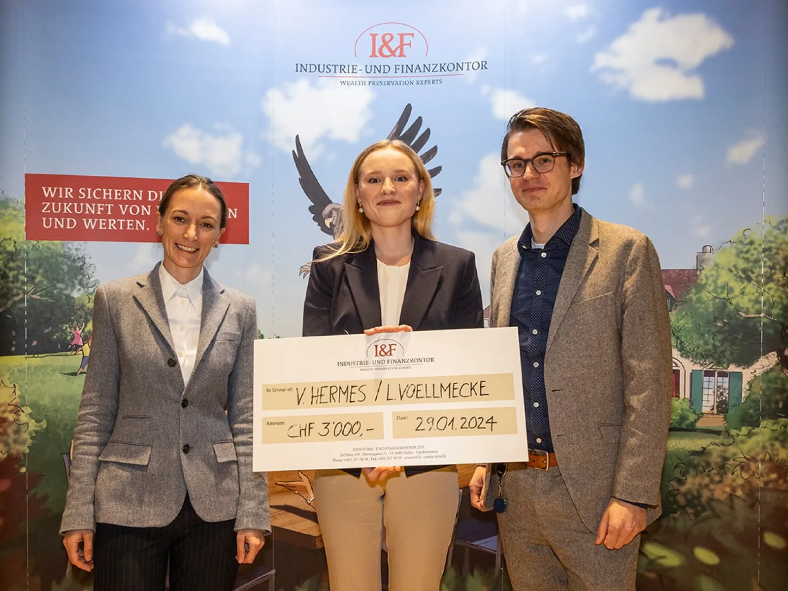 Drei Personen stehen lächelnd vor einem Hintergrund mit dem Logo der Industrie- und Finanzkontor. Eine Person hält einen großen Scheck mit der Aufschrift "CHF 3,000" und einem Datum. Im Hintergrund ist ein stilisiertes Bild mit einem Adler und einem Haus zu sehen.