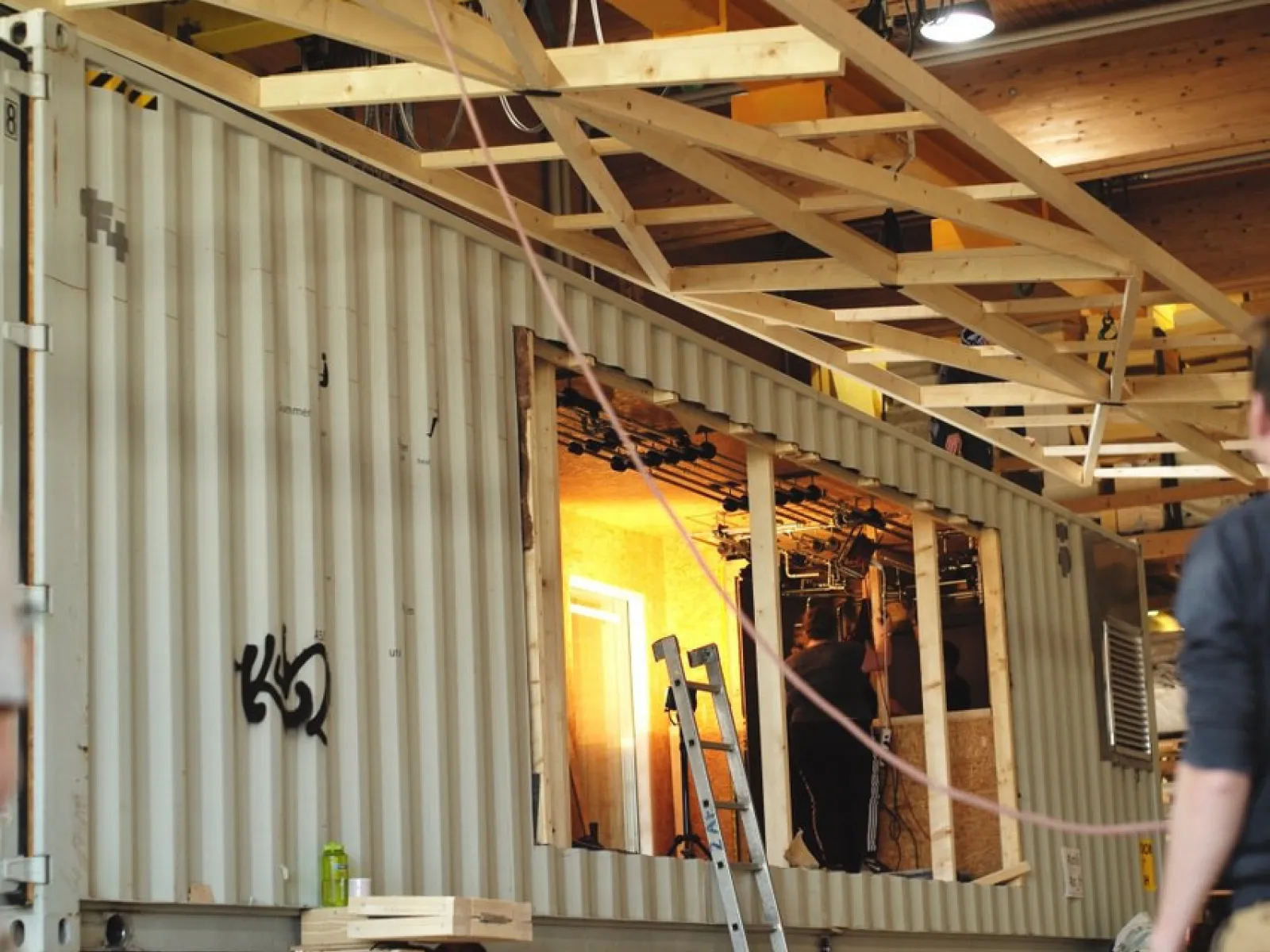 Ein großer, umgebauter Container in einer Werkhalle, mit sichtbaren Holzverstärkungen und einer Leiter, symbolisiert die flexible Nutzung des Base Camps der Universität Liechtenstein für Stadtentwicklungsprojekte.