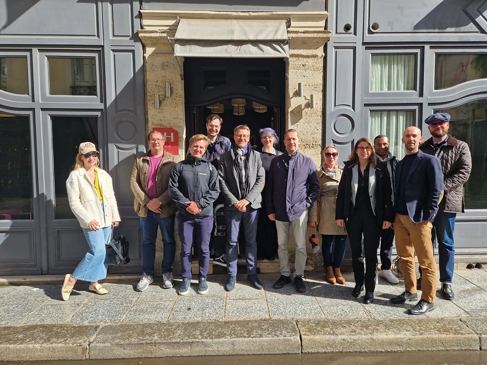 Eine Gruppe von Studierenden und Dozenten des Executive Master of Laws (LL.M.) im Wirtschaftsstrafrecht steht vor einem Gebäude in Straßburg während ihrer Studienreise zum Europarat. Sie lächeln in die Kamera und tragen verschiedene Freizeit- und Businesskleidung.