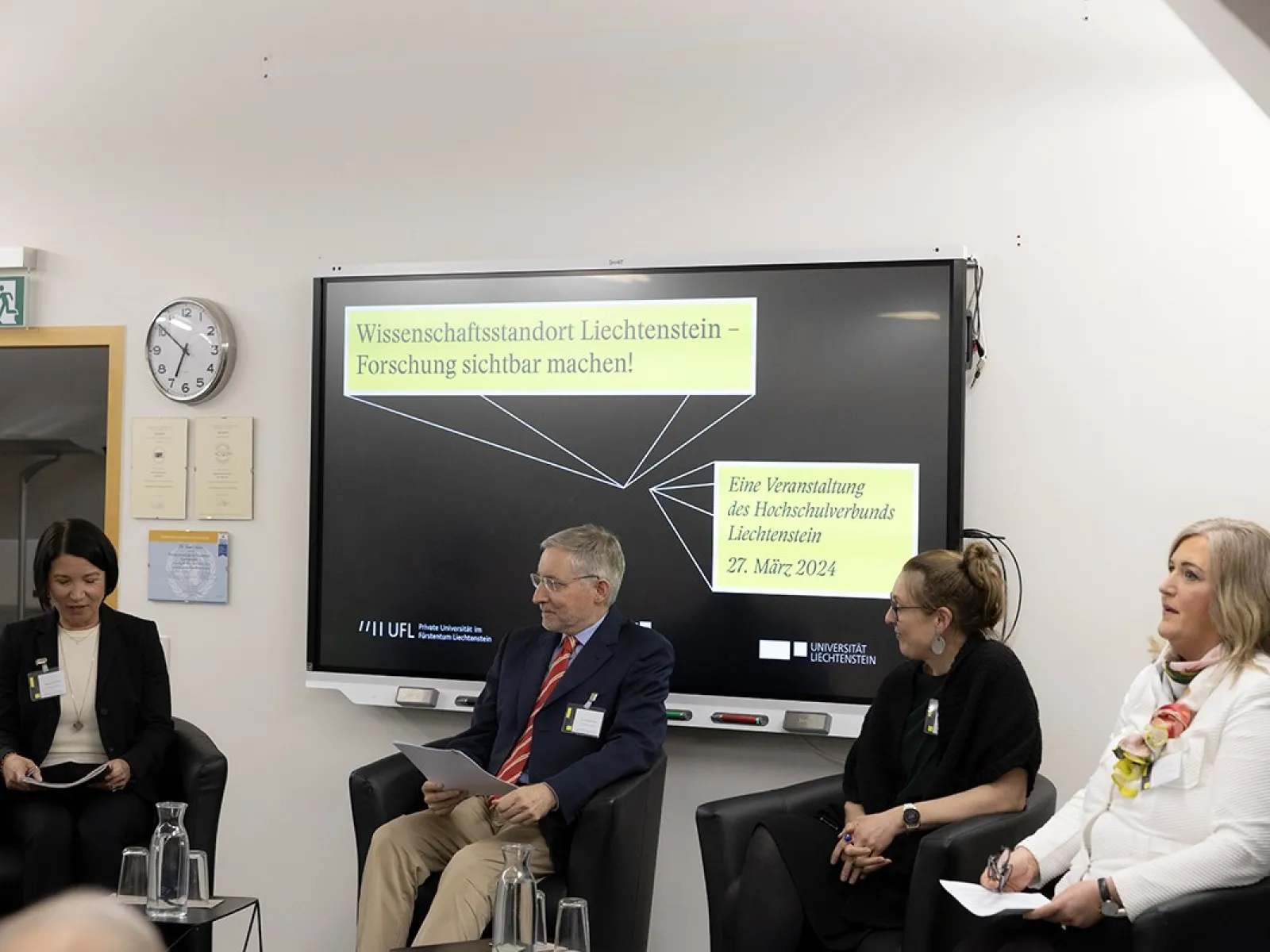 Podiumsdiskussion an der Universität Liechtenstein mit vier Personen, die auf Stühlen sitzen. Im Hintergrund ist ein Bildschirm mit der Aufschrift "Wissenschaftsstandort Liechtenstein – Forschung sichtbar machen" und dem Datum der Veranstaltung zu sehen.