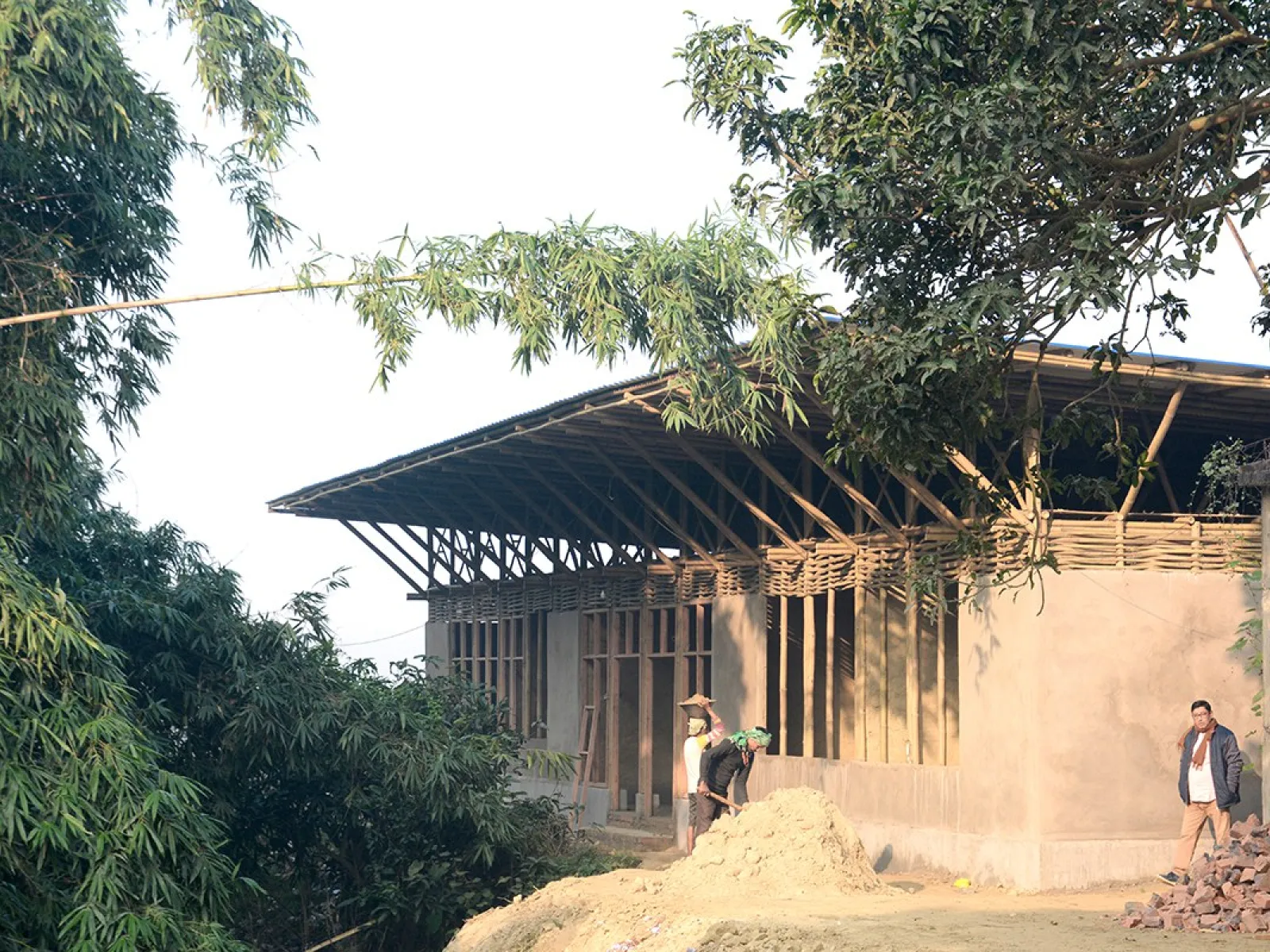 Ein im Bau befindliches Schulgebäude in Bahuarwa, Indien, umgeben von Bäumen. Das Projekt wird von Daniel Haselsberger und seiner Frau Isha initiiert und unterstützt.