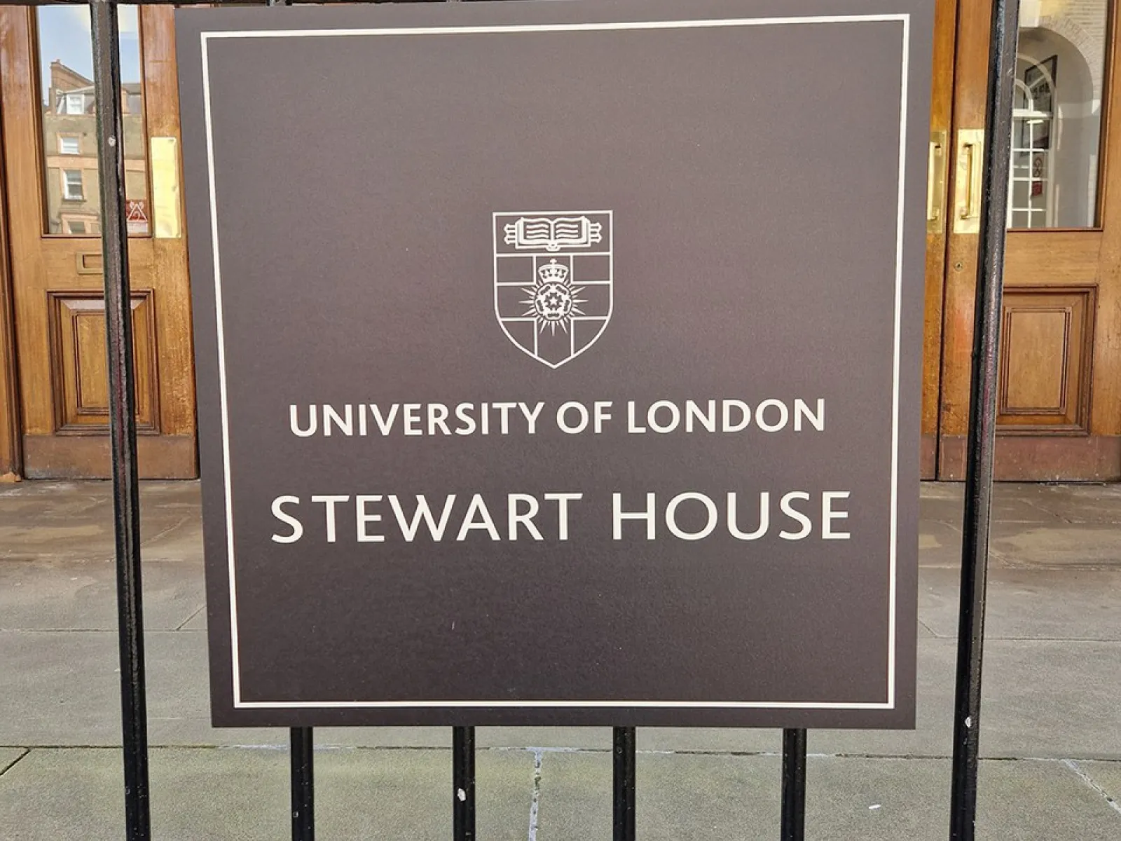 Ein Schild vor dem Eingang eines Gebäudes mit der Aufschrift "University of London, Stewart House". Im Hintergrund sind Holztüren und die Hausnummer 32 zu sehen.