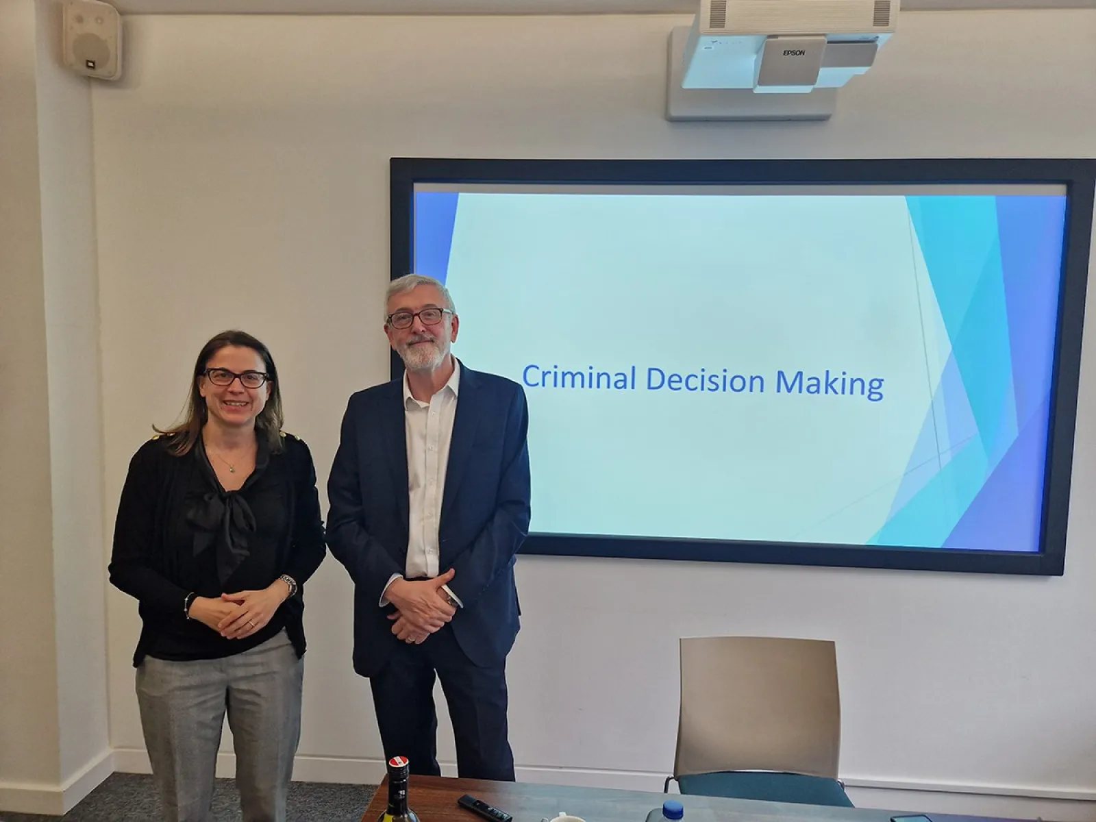 Zwei Personen stehen vor einer Präsentation mit dem Titel "Criminal Decision Making" in einem Seminarraum. Im Hintergrund ist ein Bildschirm mit dem Präsentationstitel zu sehen.