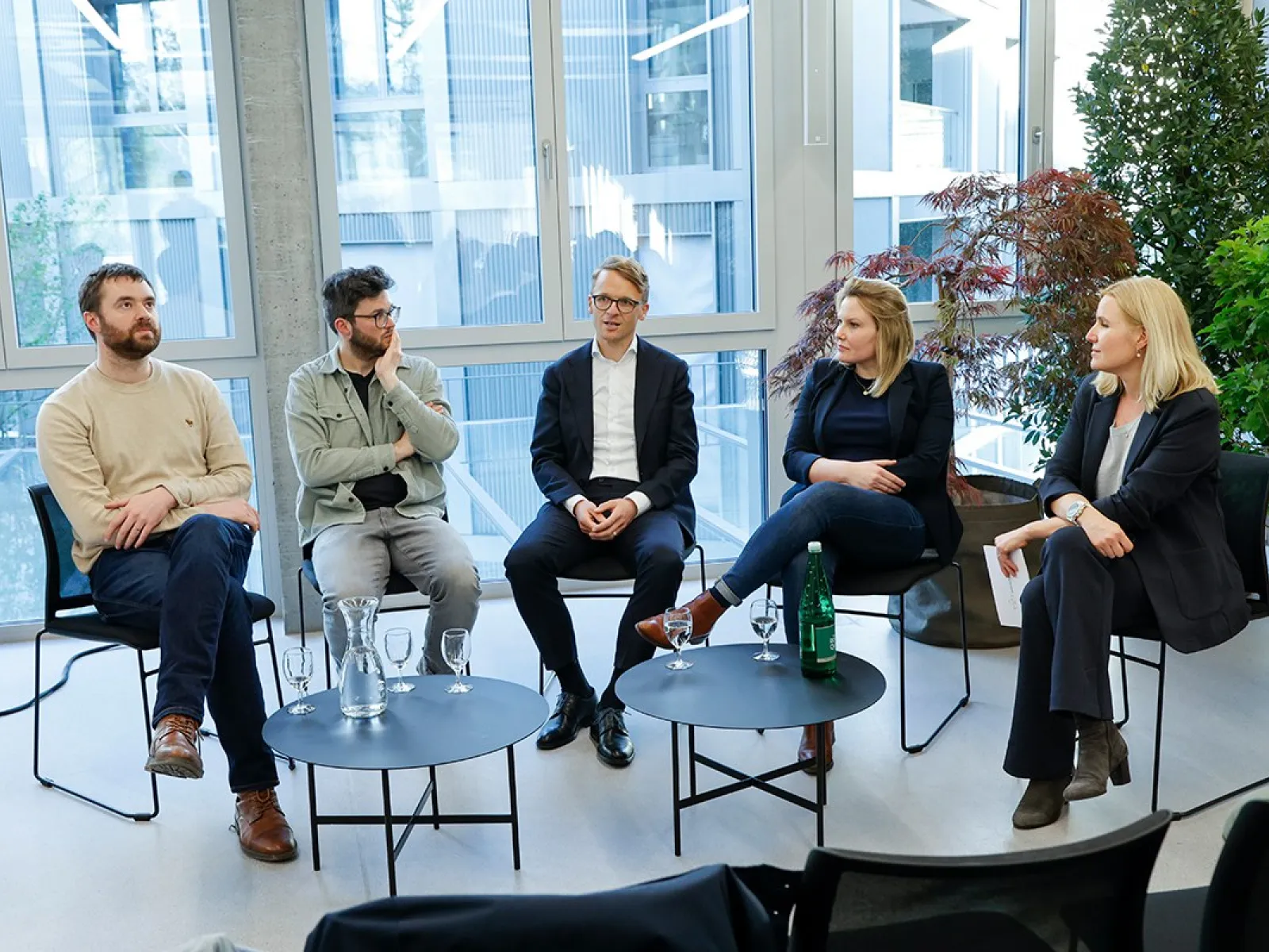 Podiumsdiskussion an der Universität Liechtenstein: Fünf Personen sitzen in einem modernen Raum mit großen Fenstern und Pflanzen, diskutieren über den Wohnungsmarkt. Vor ihnen stehen Tische mit Wassergläsern und einer Flasche.