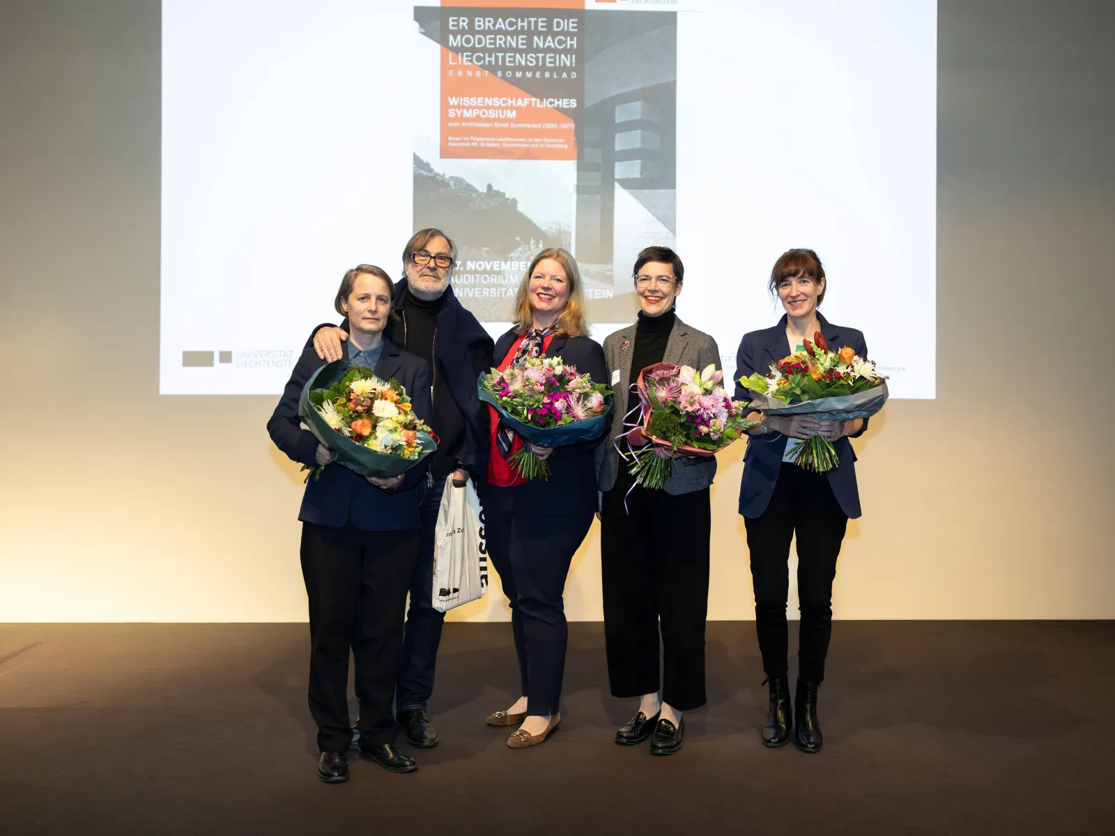 Fünf Personen auf einer Bühne mit Blumensträussen in der Hand 