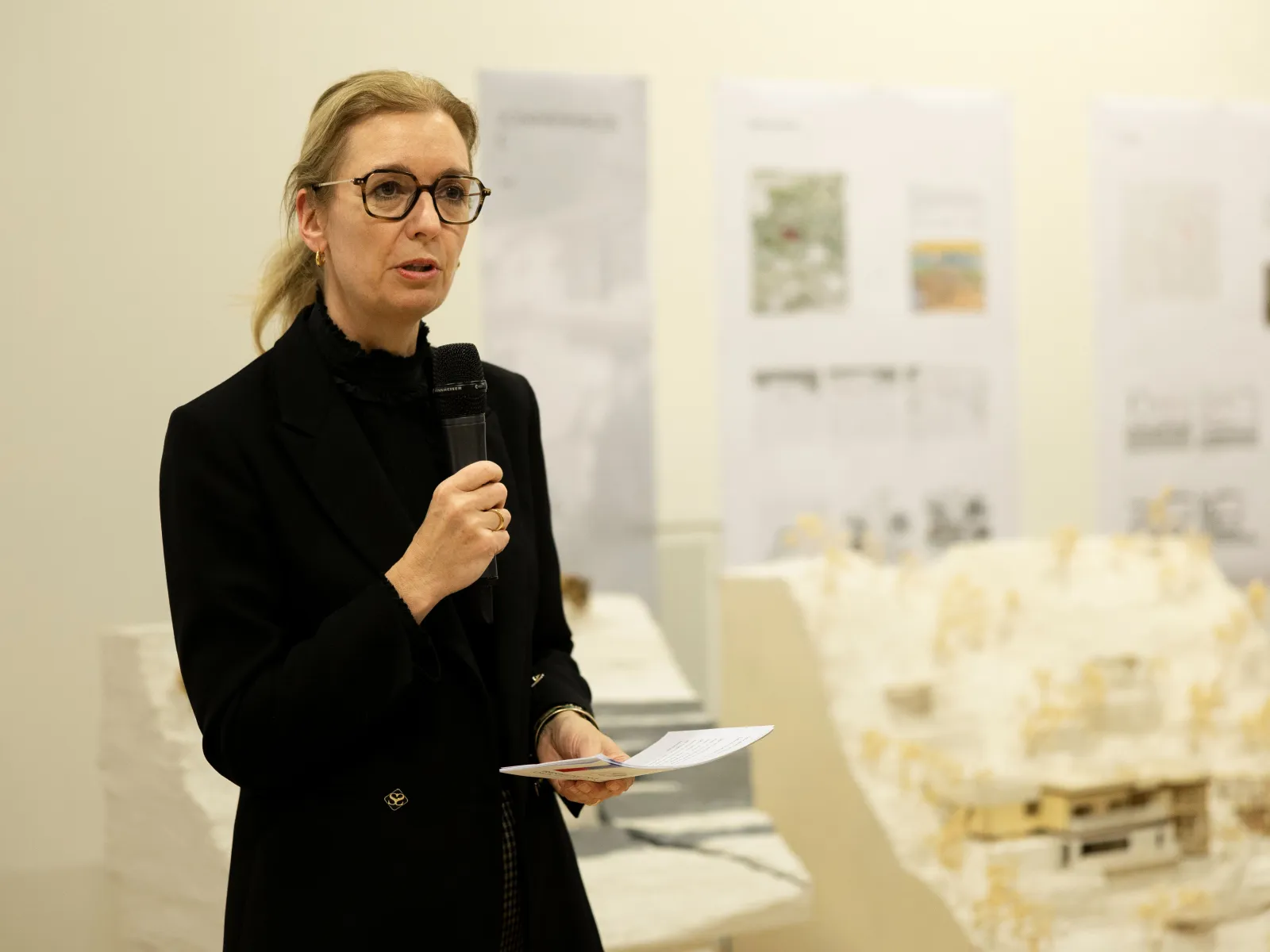 Eine Frau mit blonden Haaren und schwarzer Kleidung hält eine Rede