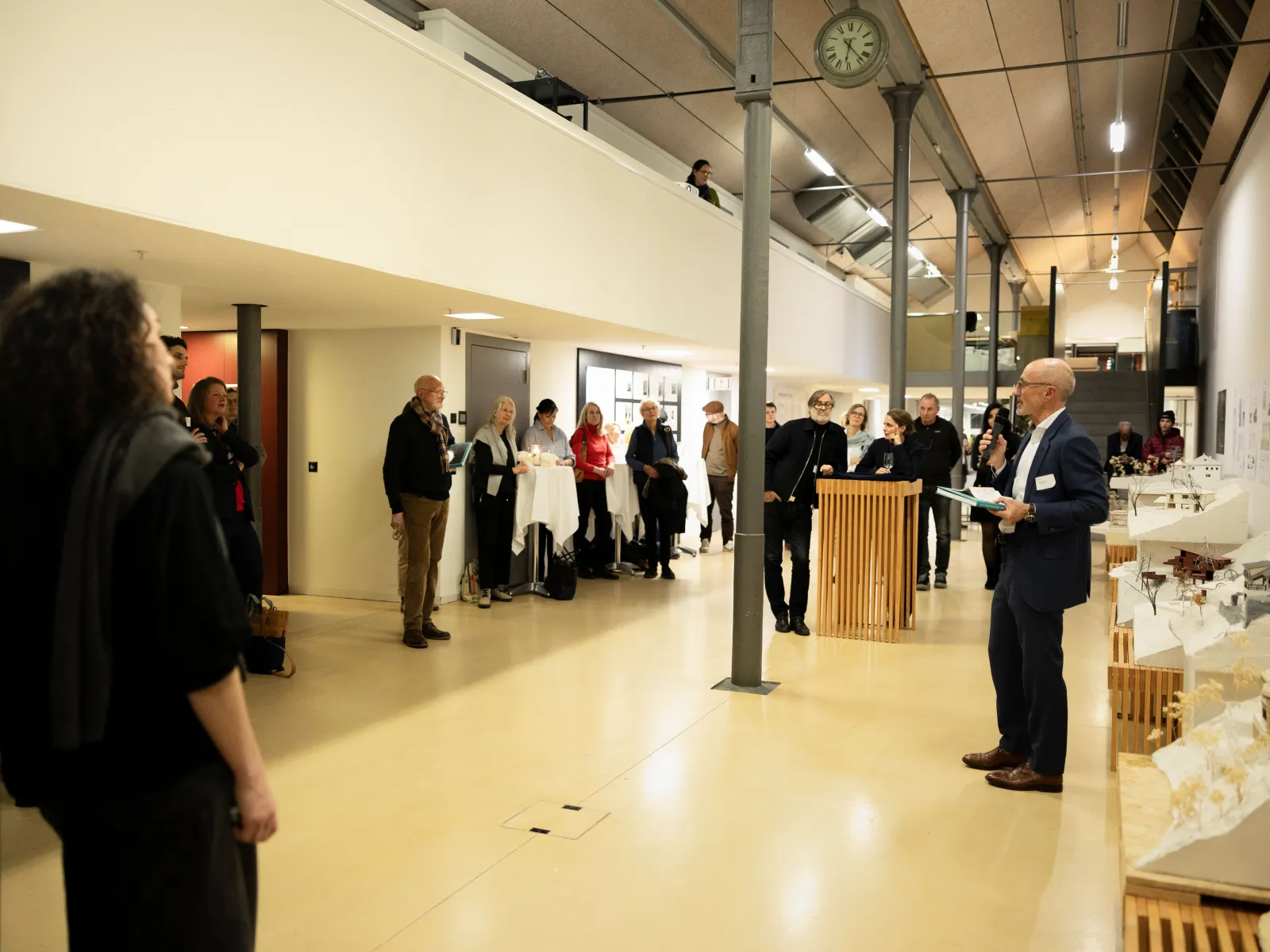 Ein Mann präsentiert vor einer Gruppe von Menschen mit einem Mikrofon in der Hand 