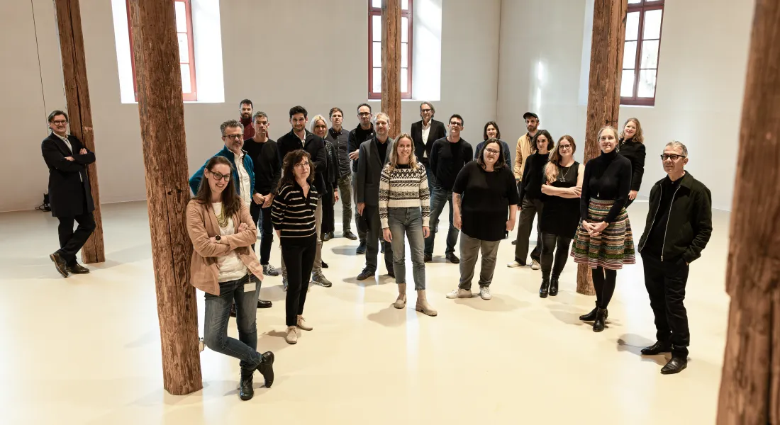 Eine Gruppe von Menschen steht in einer Halle und blickt in die Kamera. 