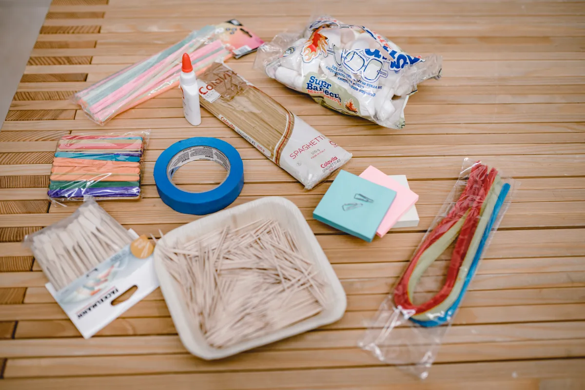 Bastelmaterialien auf Holztisch: Spaghetti, Kleber, Marshmallows und bunte Werkstoffe – Workshop an der Universität Liechtenstein