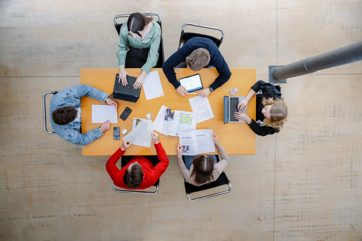 Studierende der Universität Liechtenstein arbeiten an einem Gruppentisch mit Laptops und Unterlagen im modernen Lernbereich.