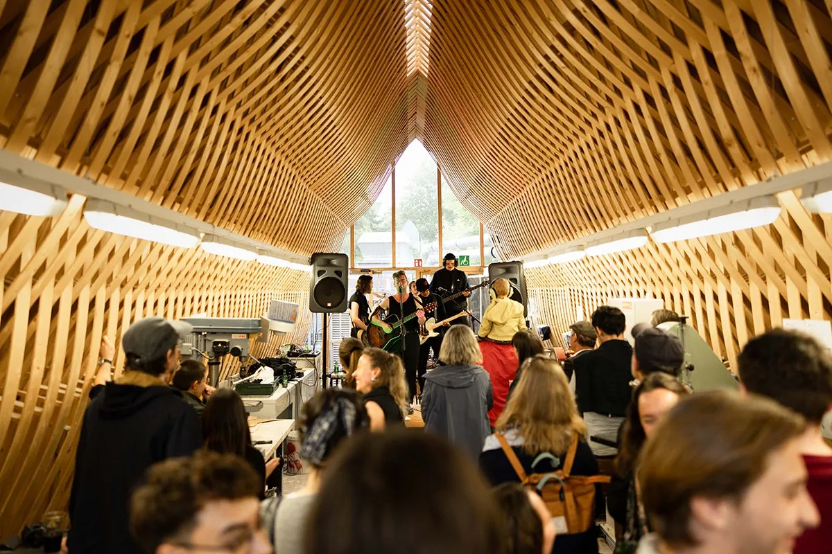 Eine Band spielt vor einem Publikum in einem architektonisch beeindruckenden Raum mit Holzgitterstruktur bei einem Event der Universität Liechtenstein.
