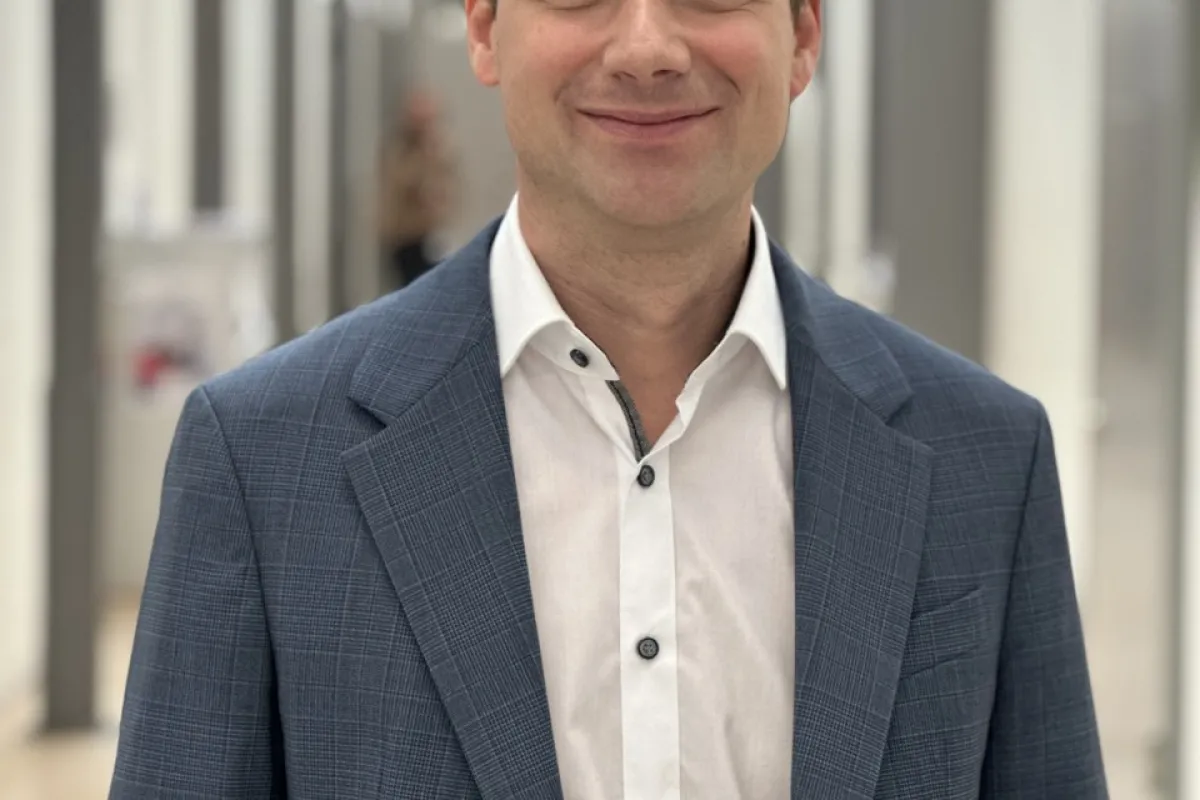 Ein lächelnder Mann in einem blauen Anzug steht in einem modernen, hellen Flur.