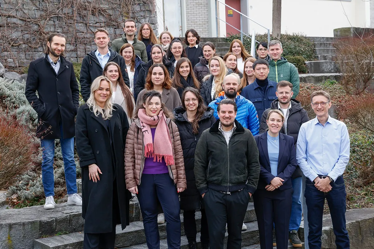 Gruppenfoto von Studierenden und Dozenten des Zertifikatsstudiengangs Compliance-Officer an der Universität Liechtenstein, aufgenommen auf einer Außentreppe. Die Gruppe lächelt in die Kamera, umgeben von winterlicher Vegetation.