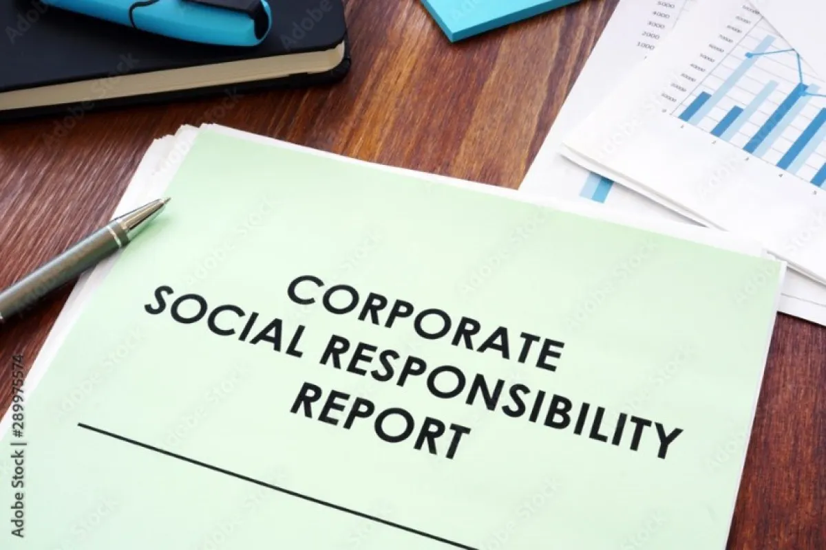 Ein Dokument mit der Aufschrift "Corporate Social Responsibility Report" liegt auf einem Holztisch, daneben ein Stift und einige Diagramme.