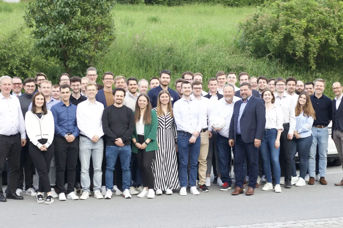 Gruppe von Doktoranden und Professoren steht lächelnd vor einer grünen Wiese bei der Universität Liechtenstein während des Internationalen Doktorandenseminars 2024.