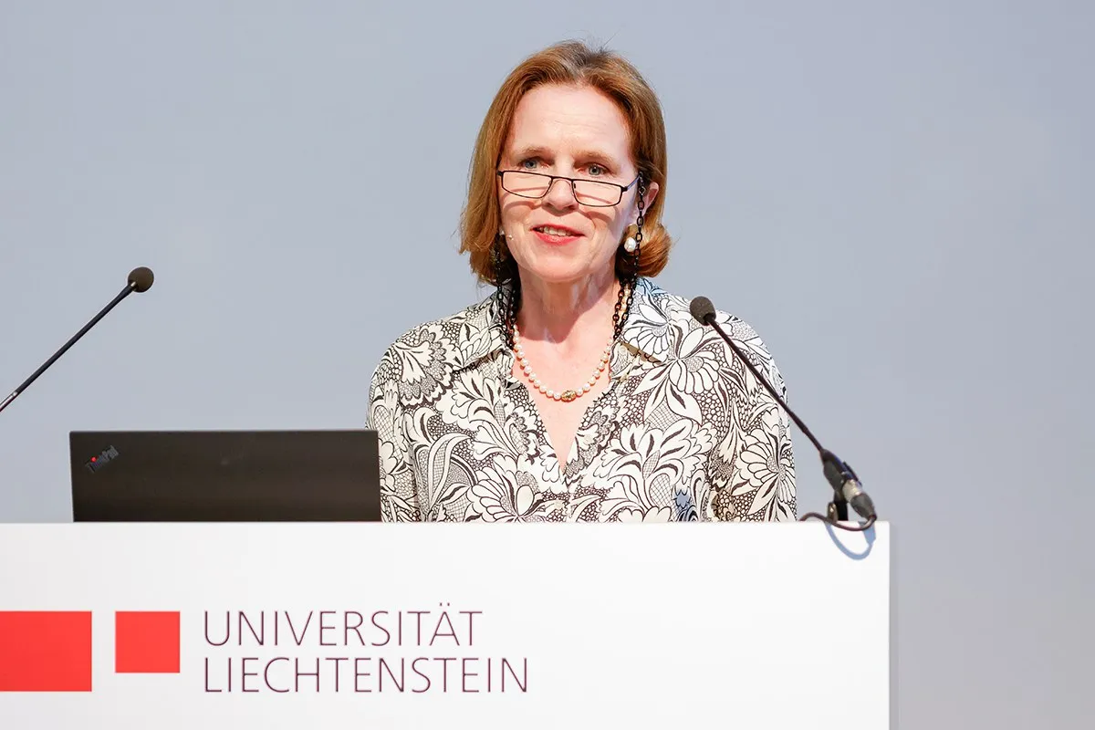 Es ist eine Frau zu sehen, welche vor einem Redepult mit dem Logo der Universität Liechtenstein steht.