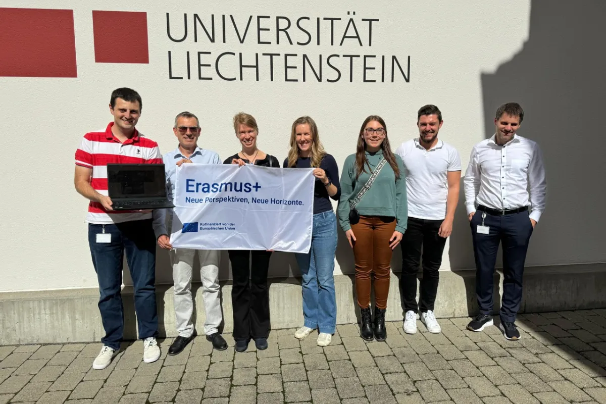 Eine Gruppe von sieben Personen steht vor einem Gebäude mit dem Schriftzug "Universität Liechtenstein". Sie halten ein Banner mit der Aufschrift "Erasmus+ Neue Perspektiven, Neue Horizonte".