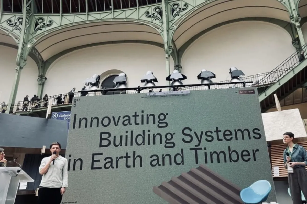 Ein Redner präsentiert auf einer Bühne vor einem großen Bildschirm mit der Aufschrift „Innovating Building Systems in Earth and Timber“ im Grand Palais, Paris. Im Hintergrund ist die beeindruckende Architektur des Veranstaltungsortes zu sehen.