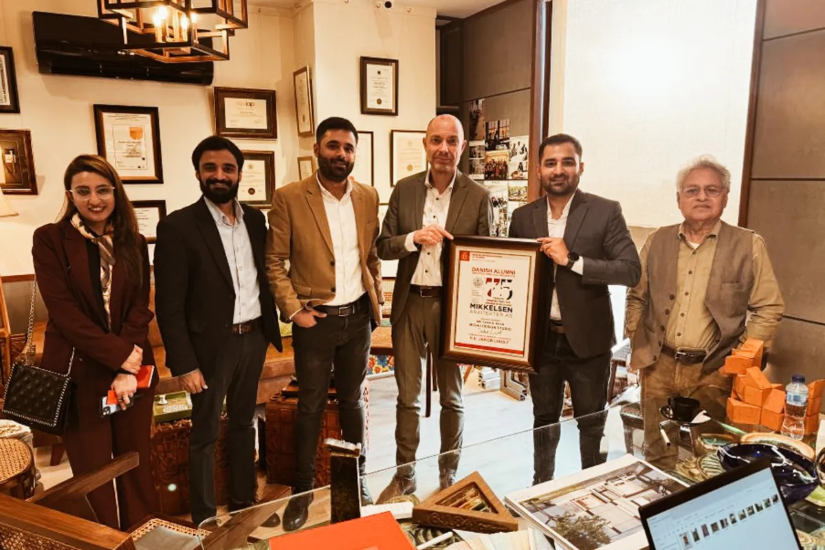 Eine Gruppe von sechs Personen steht in einem Büro, eine Person hält eine gerahmte Auszeichnung. Im Hintergrund sind Zertifikate und Auszeichnungen an der Wand zu sehen.