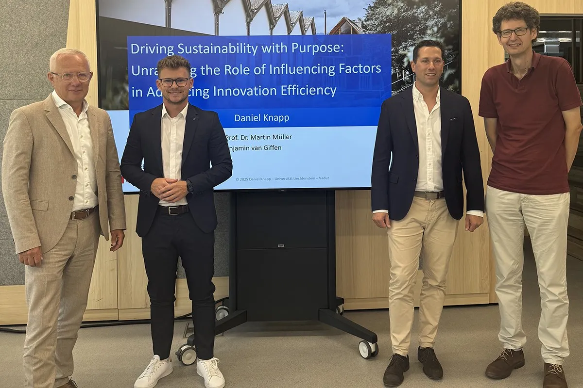 Vier Männer stehen vor einem Bildschirm, der eine Präsentation mit dem Titel „Driving Sustainability with Purpose“ zeigt. Sie tragen Business-Kleidung und lächeln in die Kamera. Der Hintergrund ist ein moderner Innenraum.