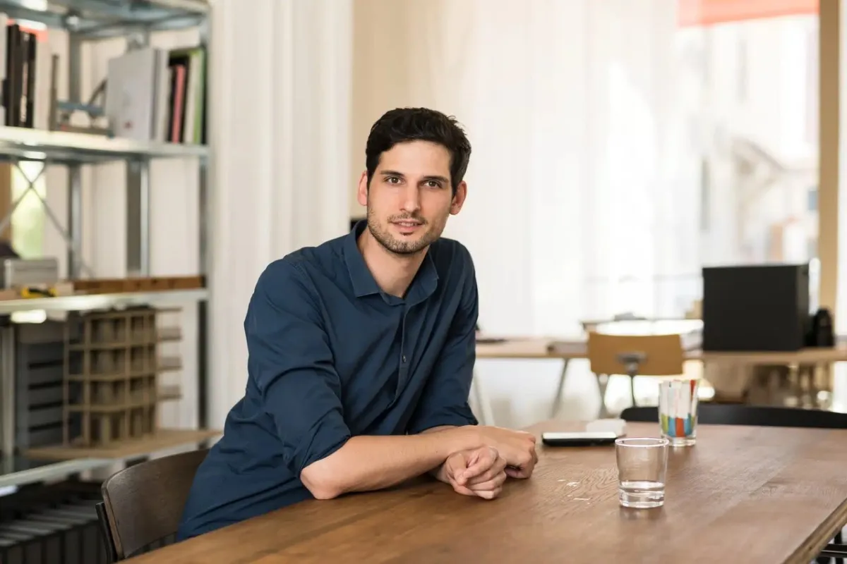 Ein Mann mit blauem Hemd sitzt an einem Tisch und hat ein Glas Wasser vor sich stehen.