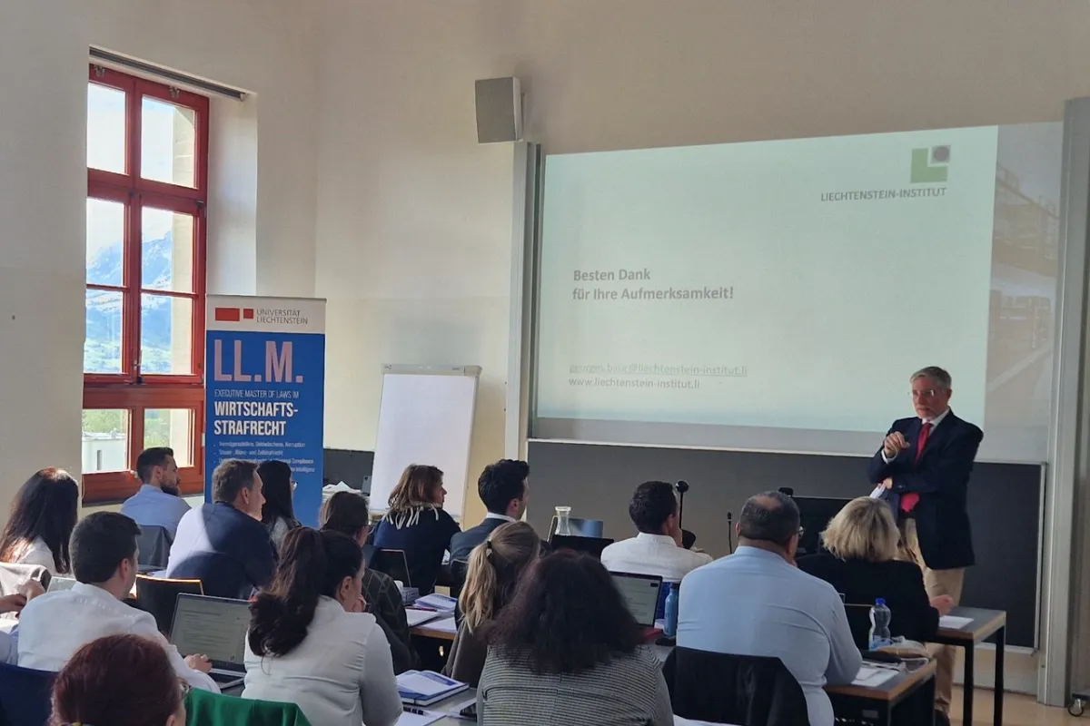 Ein Vortragender steht vor einer Gruppe von Teilnehmenden in einem Seminarraum der Universität Liechtenstein. Auf der Leinwand ist eine Präsentationsfolie mit dem Text "Besten Dank für Ihre Aufmerksamkeit!" zu sehen. Im Hintergrund ist ein Banner mit der Aufschrift "LL.M. Wirtschafts-Strafrecht" sichtbar.