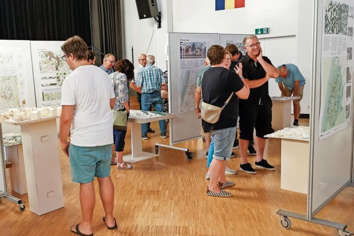 Menschen betrachten Architekturmodelle und Plakate in einer Ausstellungshalle. Die Veranstaltung zeigt studentische Projekte zur Ortsentwicklung in Ruggell, präsentiert von der Universität Liechtenstein.