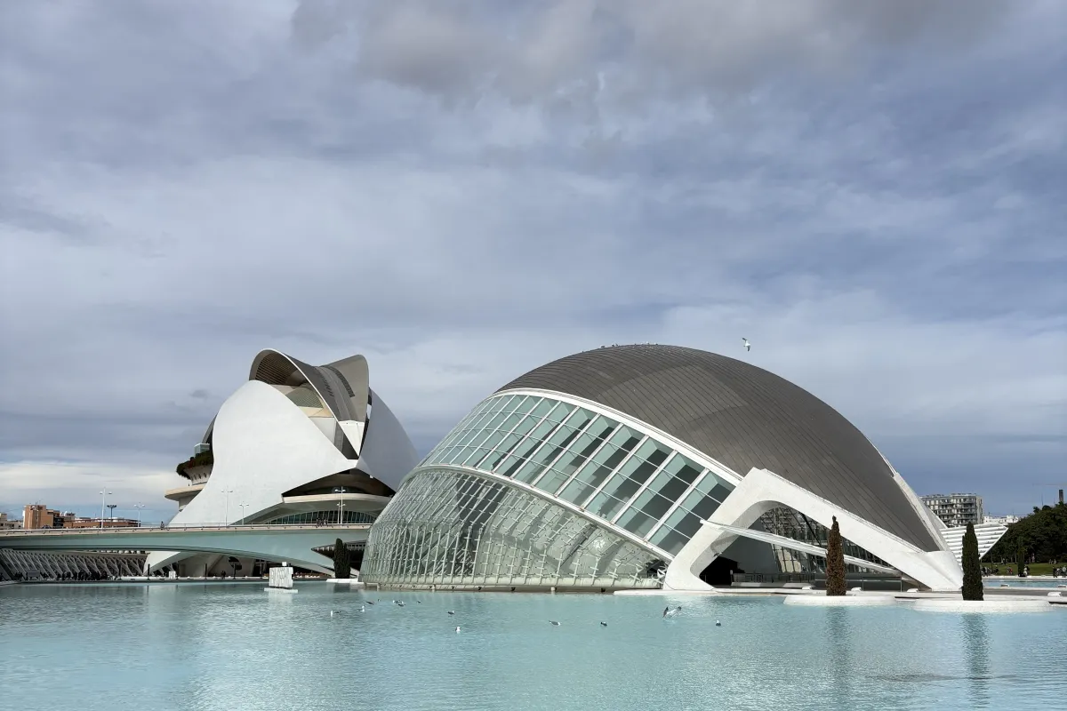 Moderne, futuristische Gebäude mit geschwungenen Glas- und Betonformen an einem großen Wasserbecken unter bewölktem Himmel.