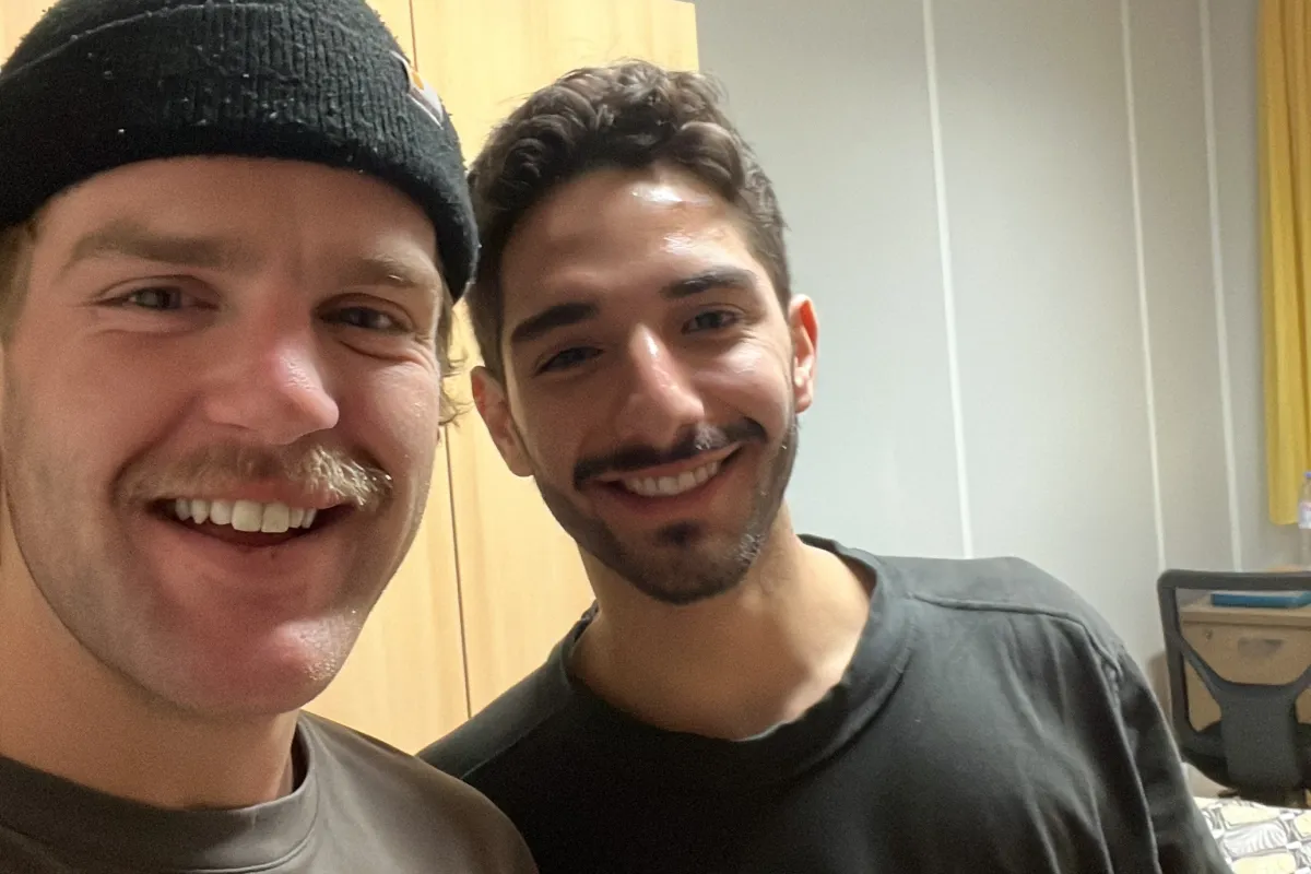 Two students smiling at the camera while holding beverage cans.