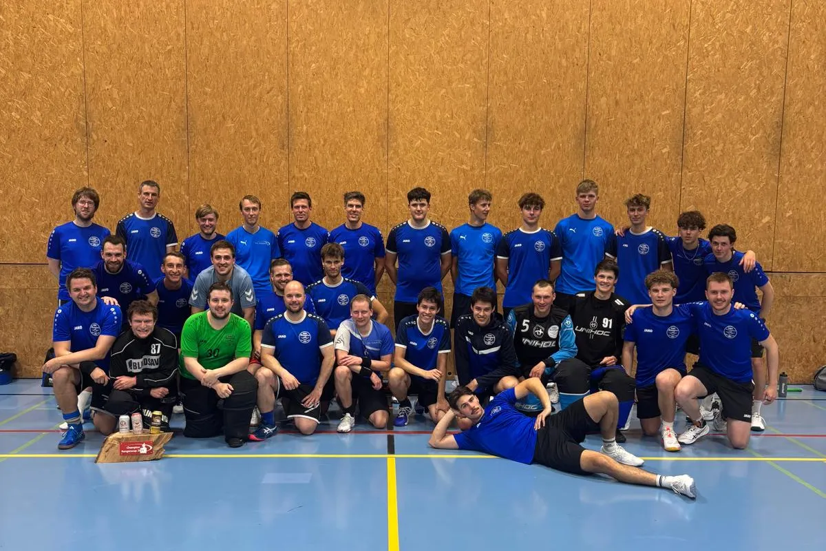 Gruppenfoto einer Handballmannschaft in blauen Trikots in einer Sporthalle.