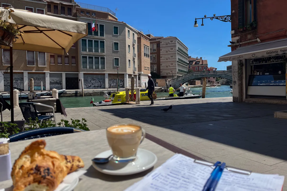 Kaffee, Croissant und Notizen auf einem Tisch an einem Kanal in Venedig.