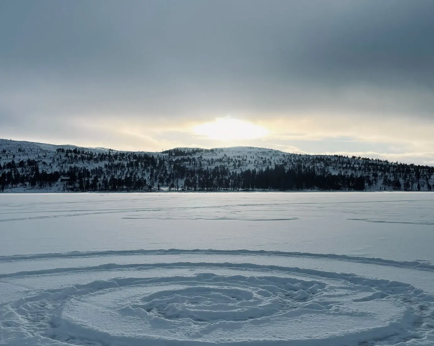 Spiralförmige Spur im Schnee auf gefrorenem See vor Hügeln.