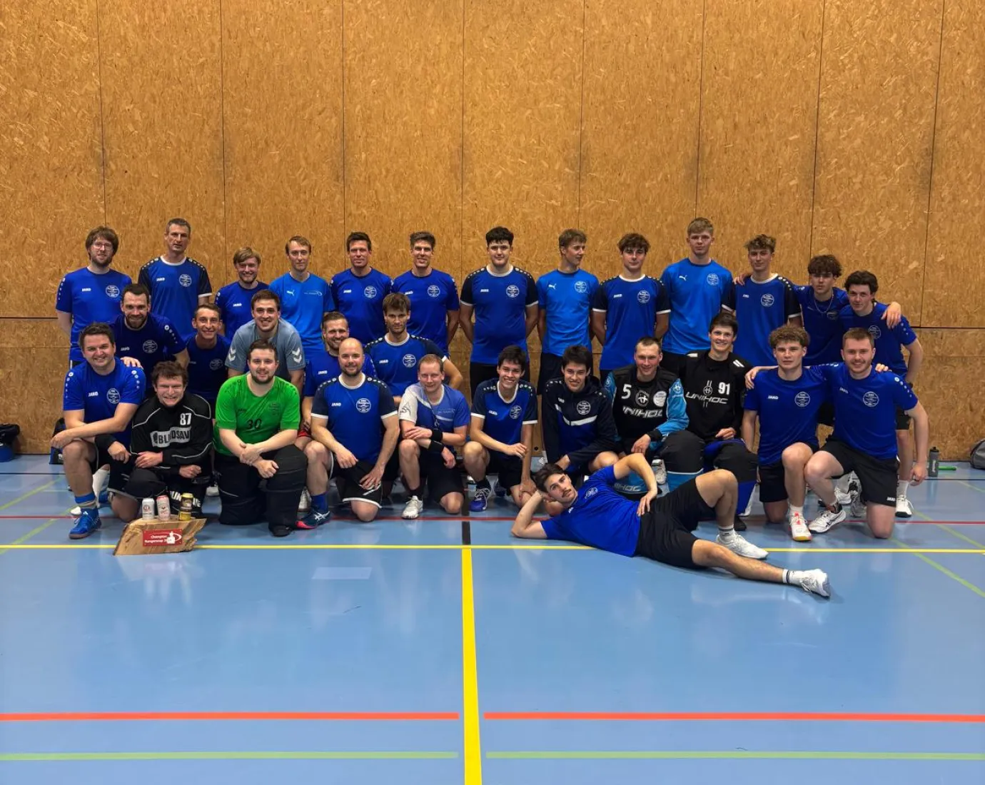 Gruppenfoto einer Handballmannschaft in blauen Trikots in einer Sporthalle.