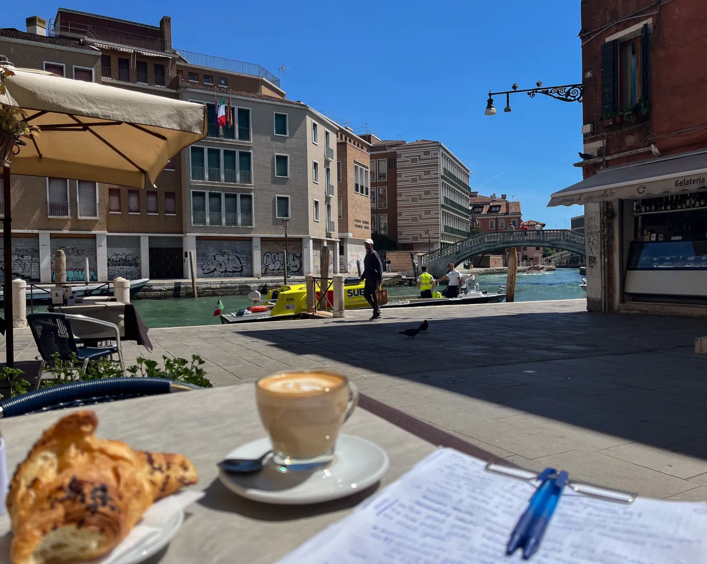 Kaffee, Croissant und Notizen auf einem Tisch an einem Kanal in Venedig.